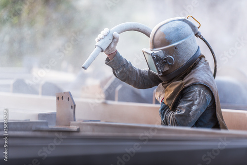 Sand blasting process, Industial worker using sand blasting process preparation cleaning surface on steel before painting in factory workshop. photo