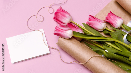 Spring mockup with pink blank paper list and pink tulip flowers bouquet on pink background top view. Beautiful floral composition for design. Flat lay