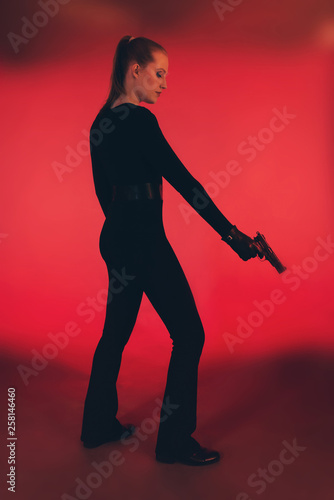 Silhouette of woman in black holding pistol. Against red background.