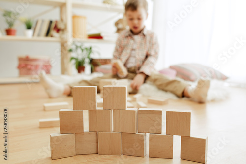 Little child sitting on the floor. Pretty boy palying with wooden cubes at home. Conceptual image with copy or negative space and mock-up for your text