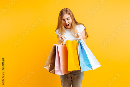 Portrait of a curious young woman , after a good shopping, looking inside the bag, isolated on a yellow background