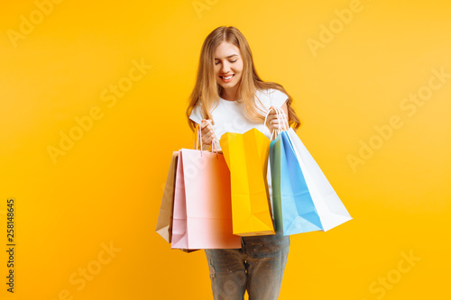 Portrait of a curious young woman , after a good shopping, looking inside the bag, isolated on a yellow background