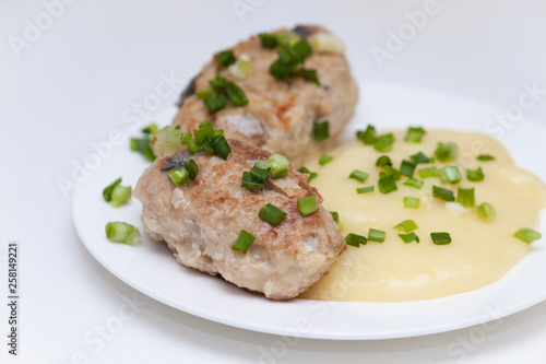 Delicious fried homemade fish cakes or cutlets on white plate with green onion and potato.