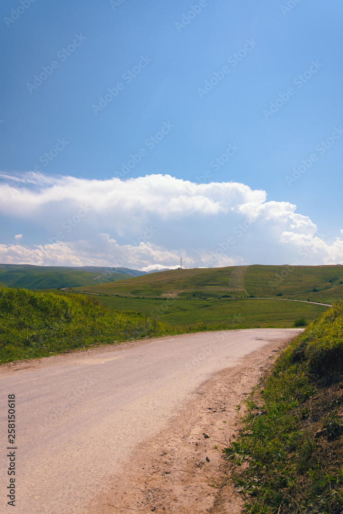Fototapeta premium Mountain road stretching into the distance among the low clouds on a summer day.