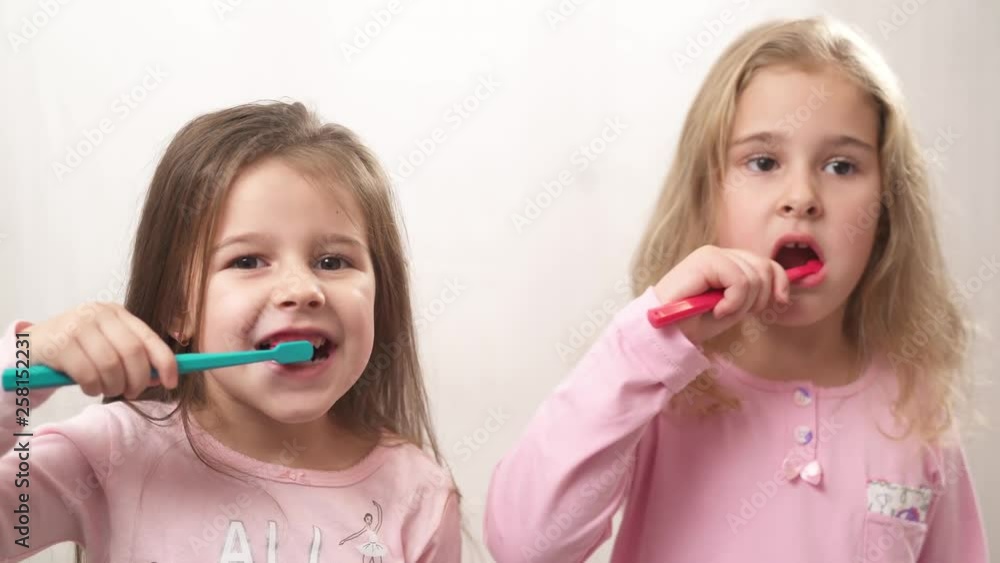 Two funny little girls cleaning their teeth with a toothbrush in the bathroom Two funny little girls cleaning their teeth with a toothbrush in the bathroom