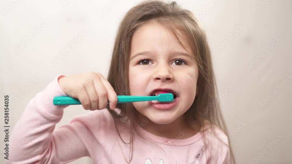 Little cute girl in pink pajamas diligently brushes her teeth with a green toothbrush Little cute girl in pink pajamas diligently brushes her teeth with a green toothbrush