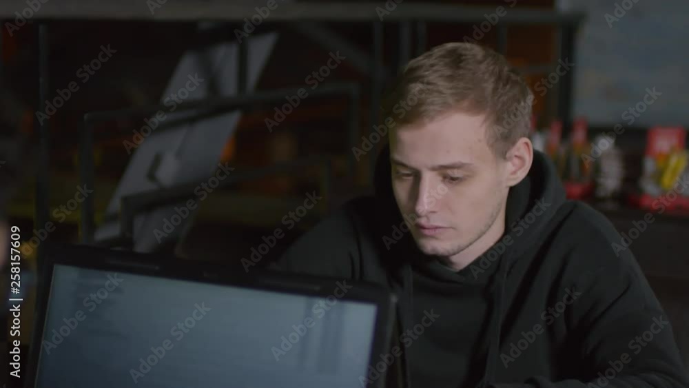 Back view of two young men in hoodie sitting at table in front of each other and creating program code on laptops Back view of two young men in hoodie sitting at table in front of each other and creating program code on laptops