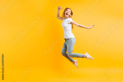Fototapeta Naklejka Na Ścianę i Meble -  Portrait of a cheerful enthusiastic girl in a white T-shirt jumping for joy on a yellow background