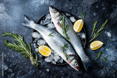 Foto Fresh raw seabass fish on black stone background with spices, herbs, lemon