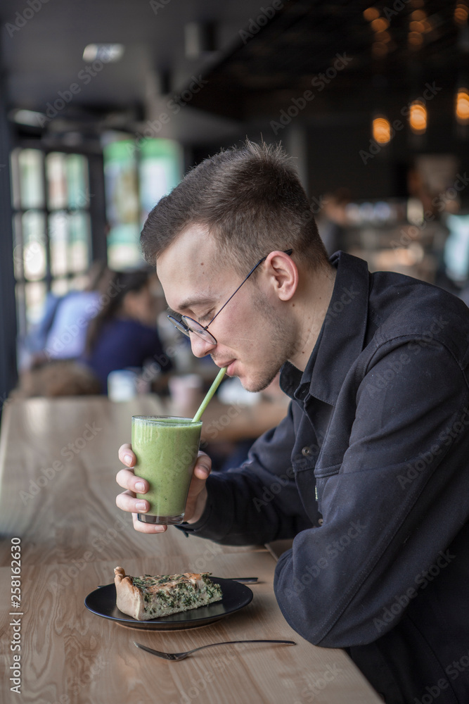 Young stylish man enjoys a cake and a drink while sitting in a cafe with large windows Young stylish man enjoys a cake and a drink while sitting in a cafe with large windows