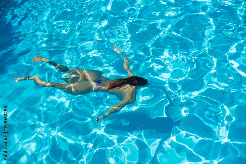 Obraz premium Over head rear view of an attractive young woman swimming under water and wearing in bikini
