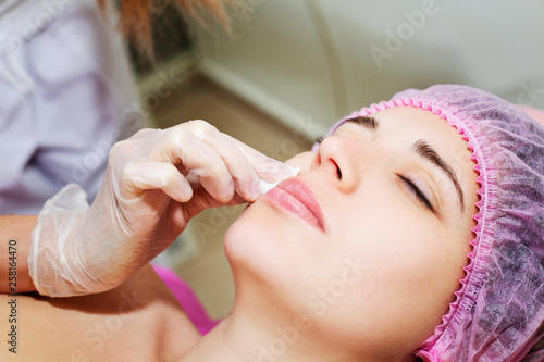 Depilation with hot wax mustache in the beauty salon. Young woman receiving facial epilation close up. Cosmetologist removes hair on face. Beauty salon, mustache depilation.