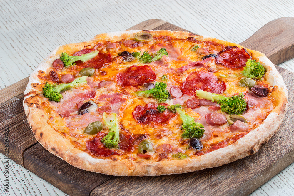 Pizza with ham, sausages, chorizo, broccoli and olives on a wooden board
