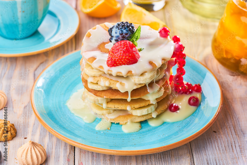 Stack of homemade pancakes with strawberrie, banana and red currant on a blue plate Stack of homemade pancakes with strawberrie, banana and red currant on a blue plate