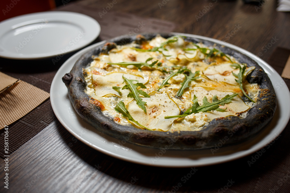 Black cheese pizza served on table in restaurant