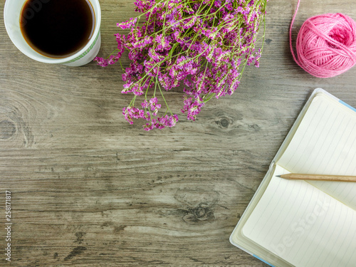 Flat lay,top view grey wooden desk with stationery including notebook and pencil with a cup of coffee,flowers  and copy space 
