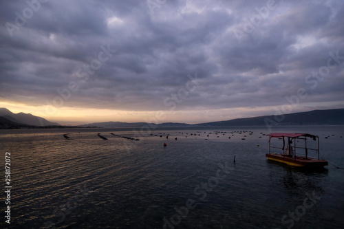 Shellfish breeding on Mediterranean sea. Mussel farm with boat on Adriatic coast. Oyster beds at low tide in oyster farm in early morning golden light. Dramatic sky with grey clouds over calm water.