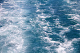 Turbulence made by foam of sea water from a high-speed yacht on surface of sea. Blue sea waves with lot of sea foam. Surface of sea with waves, splash, foam and bubbles, blue background and wallpaper.