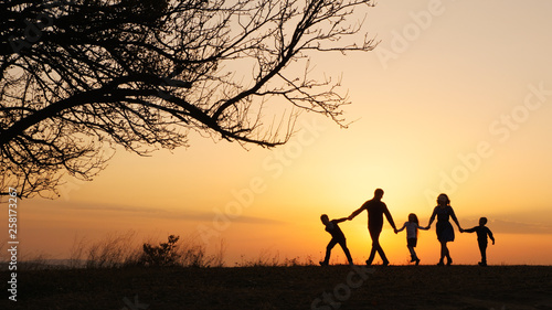 Silhouettes of happy family walking together in the meadow during sunset