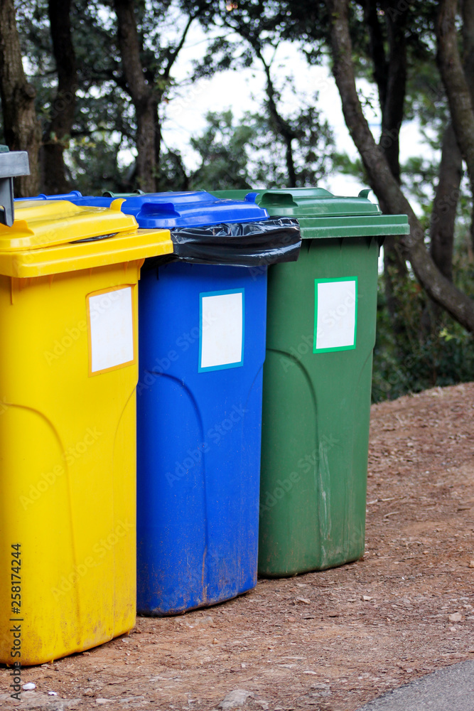 Trash can, garbage bin, recycling bin in tourist complex resort, waiting to be picked up by garbage truck. Blue, yellow and green containers for waste sorting, sort garbage for metal, paper and glass.