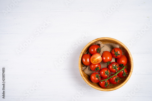 Fresh cherry tomatoes in a wooden plate on a white wood background.