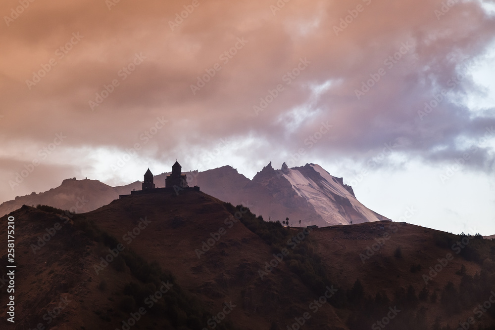 Lonely monastery in mountains. Trinity Church in mountains near village of Gergeti. A landscape with gloomy sky and dark mountains. Caucasian mountains. Tourism and travel in Georgia.