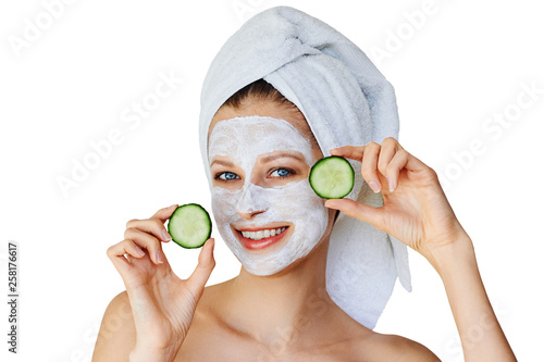 Beautiful young woman with facial mask on her face holding slices of cucumber. Skin care and treatment, spa, natural beauty and cosmetology concept, isolated over white background