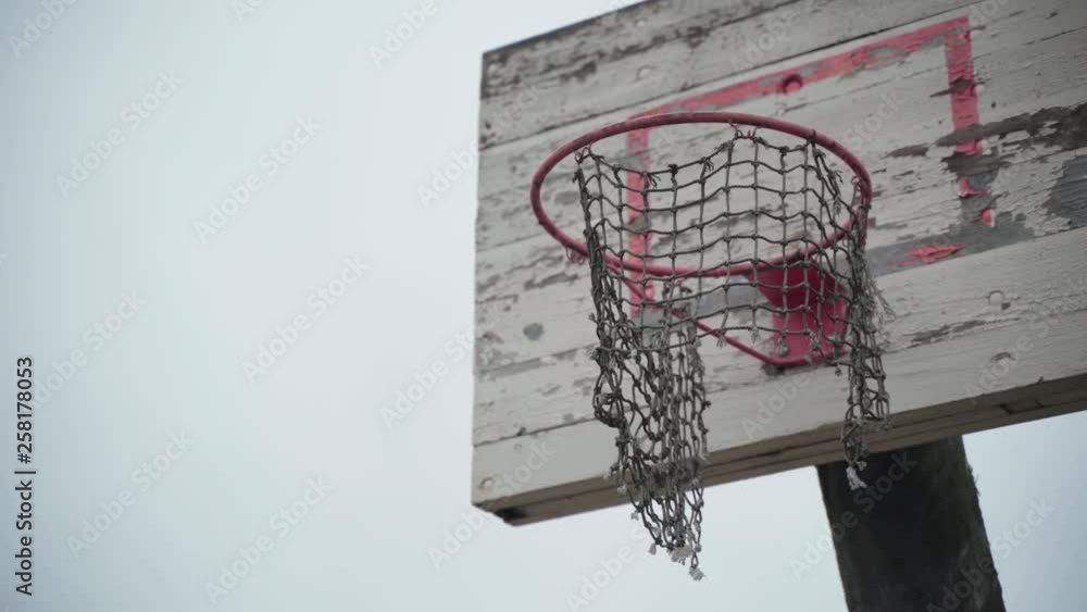 Old basketball hoop with torn net hanging in wind and peeled off paint Old basketball hoop with torn net hanging in wind and peeled off paint