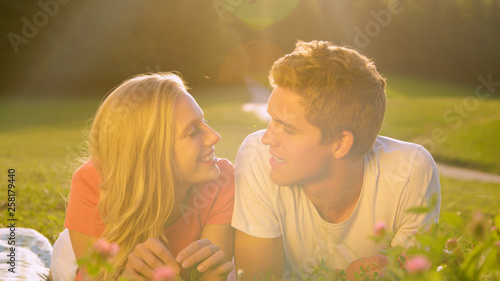 CLOSE UP: Young man and woman talking while lying in the tranquil sunny meadow.
