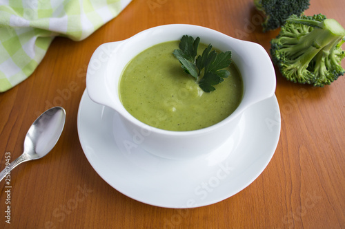 Vegetarian broccoli puree soup in th white bowl on the light brown wooden background