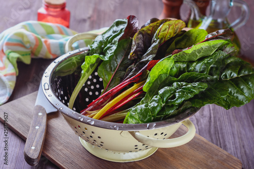 A lot of colorful eaves of chard are drained in a colander after has been rinsed in cold water to prepare salad with others ingridients