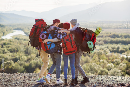 Fotografi View from back of four hipster friends traveler holding hands standing on the top of mountain on sunset background