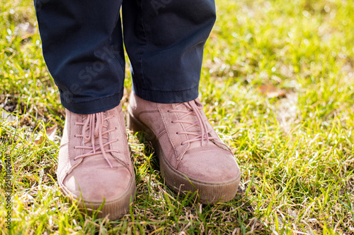 Female legs in jeans and pink sneakers on green grass, spring day