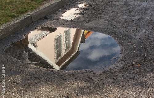 A small detached house with a pink facade is reflected in a puddle after rain