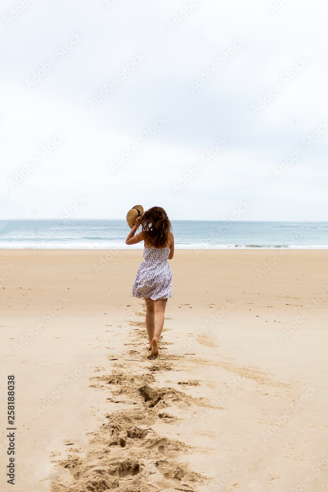 Girl in hat and white dress running towards water on the empty beach Girl in hat and white dress running towards water on the empty beach