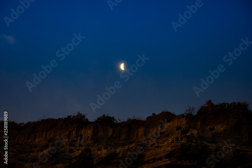  Night. Rocks, bird caves, parrot reserve, Patagonia, Argentina. Colors: earth, blue and shores in clouds. Moon over the horizon.