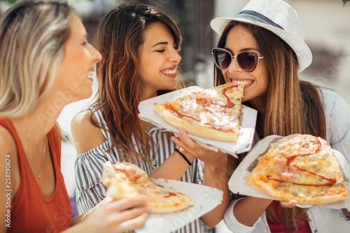 Three beautiful young women eating pizza after shopping  having fun together.