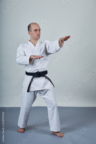 A man in karategi performs formal karate exercises on a gray cover