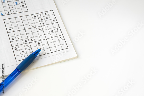 flat lay sudoku puzzle book with blue pen, against white background. space for text