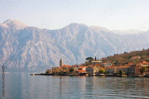 Beautiful Mediterranean landscape with a small seaside village in the background of the mountains. Montenegro, Adriatic Sea. View of Bay of Kotor and Stoliv village on sunny winter day