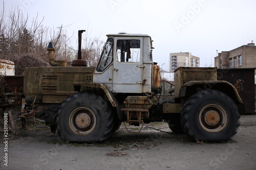 A large, rusty, old tractor on the territory of an abandoned factory.