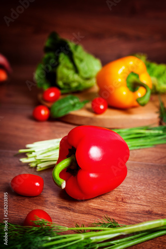 Red, yellow pepper and other vegetables on a brown wooden background.