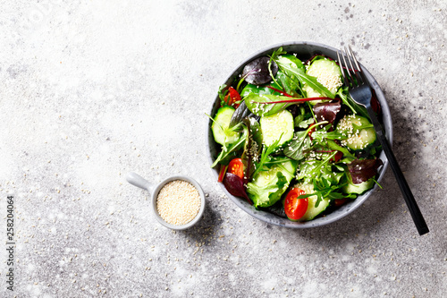 Vegetable salad in a glass bowl with greens, olive oil and sesame  on a gray background.Vegetarian. Concept for a tasty and healthy meal. Copy space for Text.Top view.