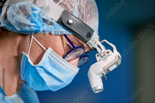 Close up portrait of female surgeon doctor wearing protective mask and hat during the operation. Healthcare, medical education, surgery concept.