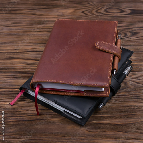 Brown and black handmade leather notebook covers with notebook and pen inside on wooden background. Stock photo of luxury business accessories.