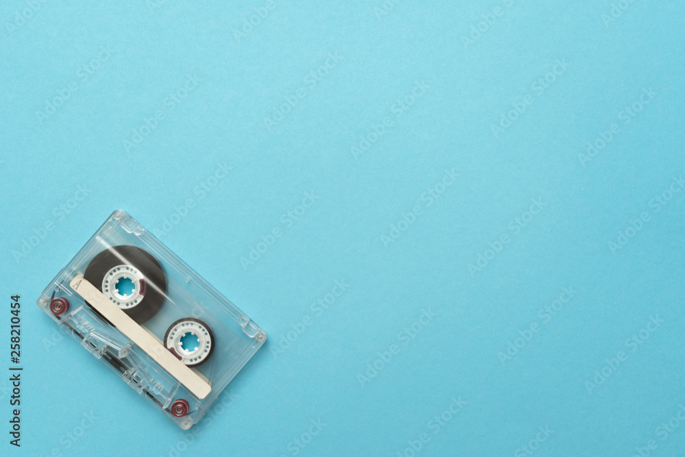 Fototapeta premium Old audio cassette in the left-down corner on blue background. Place for text.