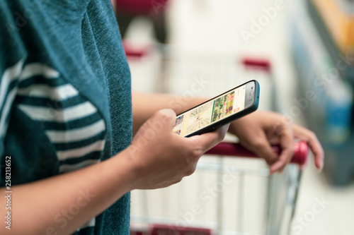 women Hand holding smartphone with blur in supermarket background photo