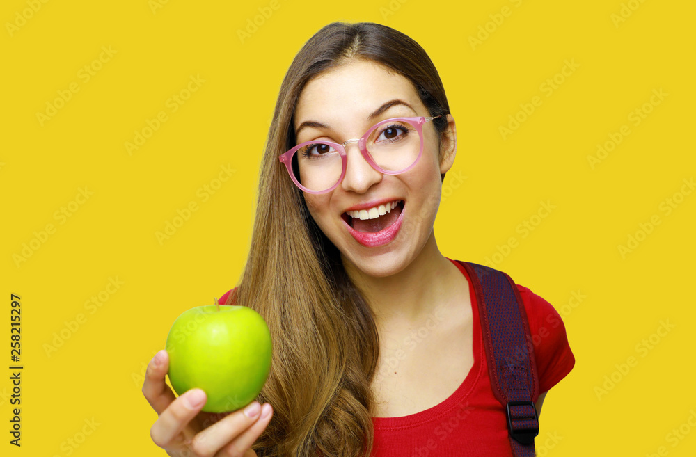 Portrait of a smiling nerd happy girl with glasses and green apple in her hand isolated over yellow background Portrait of a smiling nerd happy girl with glasses and green apple in her hand isolated over yellow background