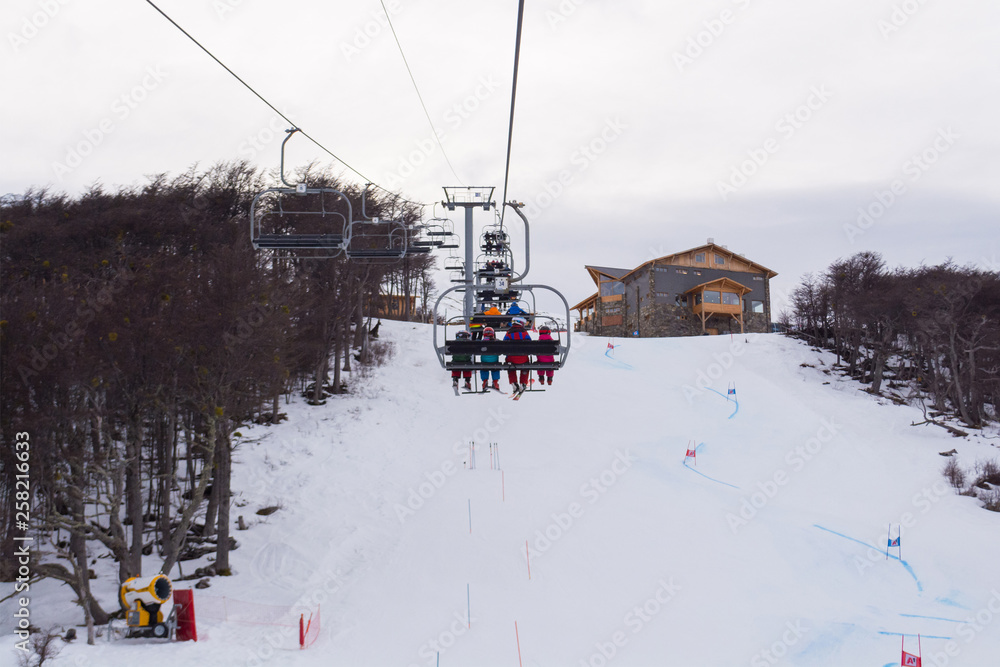 Back view of a full moving lift in Castor ski center, on a cloudy winter day, with a big practice and racing slope below and a restaurant on the background, with copy space for text. Ushuaia Argentina Back view of a full moving lift in Castor ski center, on a cloudy winter day, with a big practice and racing slope below and a restaurant on the background, with copy space for text. Ushuaia Argentina