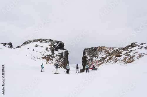 Center front view of a gap in the rocky mountains, with skiers talking and waiting on a ski slope, on a cold winter cloudy day. In Castor ski center, Ushuaia, Tierra del Fuego, Argentina.